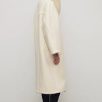 Side view of ivory regino coat on model wearing low heels, against a white background.