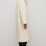 Side view of ivory regino coat on model wearing low heels, against a white background.