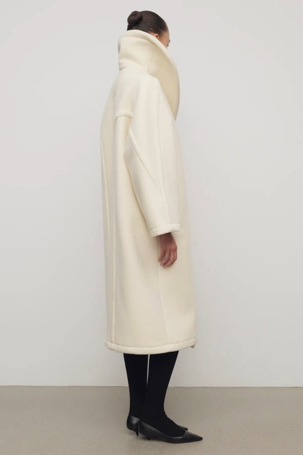 Side view of ivory regino coat on model wearing low heels, against a white background.