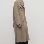 Side view of biege grey rhydian coat on model wearing black pants, against a white background.