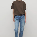 Front view of indigo riaco jean on model wearing brown shirt and sneakers, against a white background.