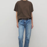 Front view of indigo riaco jean on model wearing brown shirt and sneakers, against a white background.