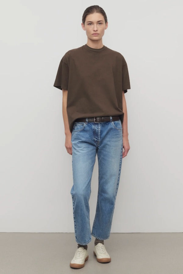 Front view of indigo riaco jean on model wearing brown shirt and sneakers, against a white background.