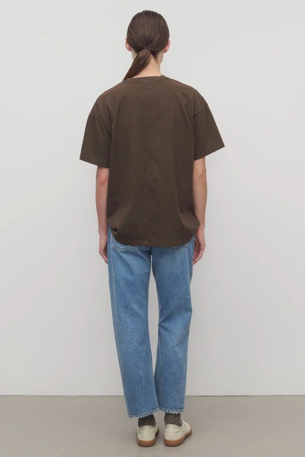 Back view of indigo riaco jean on model wearing brown shirt and sneakers, against a white bakground.