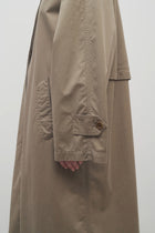 A model wears a taupe long trench coat and viewpoint is zoomed in on side angle.