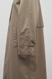 A model wears a taupe long trench coat and viewpoint is zoomed in on side angle.