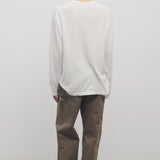 Back view of taupe sharka pant on model wearing white t-shirt and slides, against a white background.