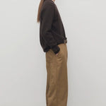 Side view of dark sand sharka pant on model wearing black top, against a white background.