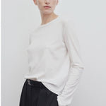 Front slanted view of white sherman t-shirt on model wearing black trousers, against a white background.