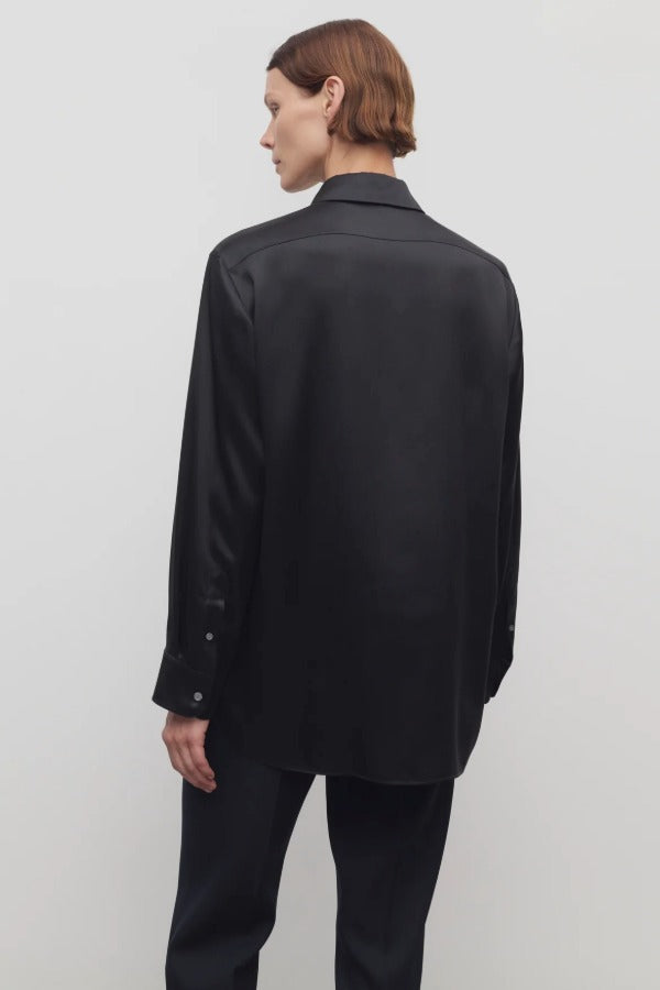 Back view of black sisilia shirt on model wearing black pants, against a white background.