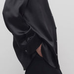 Side closeup view of black sisilia shirt on model wearing black pants, against a white background.