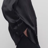 Side closeup view of black sisilia shirt on model wearing black pants, against a white background.