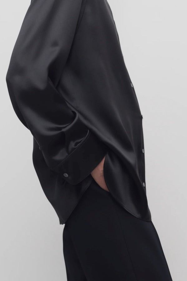 Side closeup view of black sisilia shirt on model wearing black pants, against a white background.