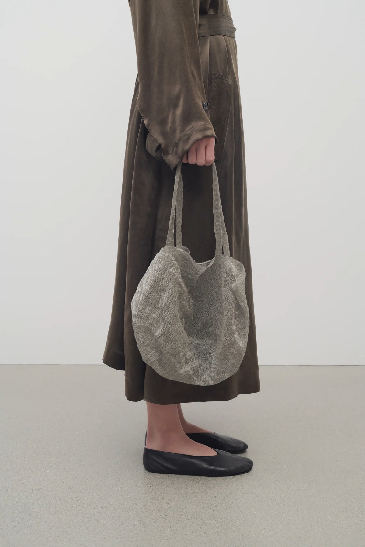 Front view of steel mesh bag on white background, with model wearing a brown dress and black ballet flats.