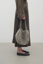 Front view of steel mesh bag on white background, with model wearing a brown dress and black ballet flats.