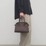 Front view of deep brown soft margaux 10 bag on model wearing black shirt, khaki pants and loafers, against a white background.