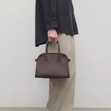 Front view of deep brown soft margaux 10 bag on model wearing black shirt, khaki pants and loafers, against a white background.