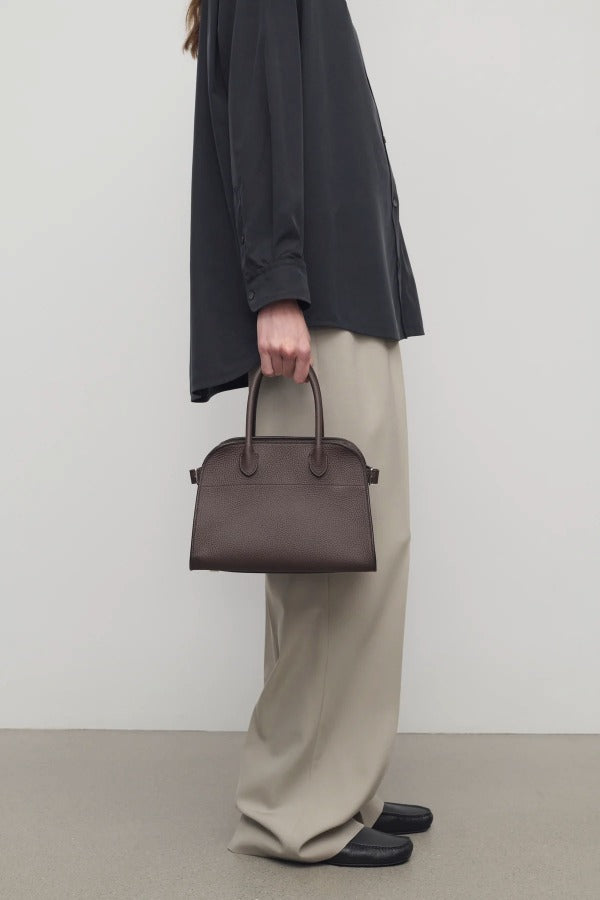 Front view of deep brown soft margaux 10 bag on model wearing black shirt, khaki pants and loafers, against a white background.