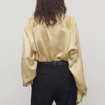 Back view of sand takara shirt on model wearing black pants and belt, against a white background.