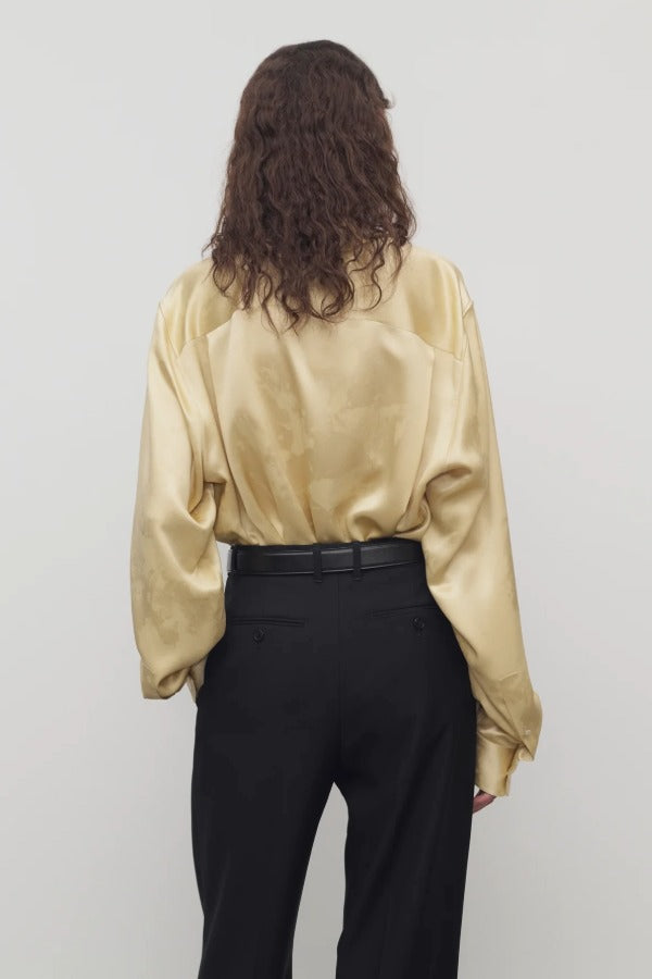 Back view of sand takara shirt on model wearing black pants and belt, against a white background.