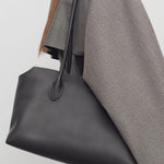 Front view of dark brown terrasse bag on model wearing grey coat, against a white background.