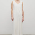 Front view of light-brown-haired model  in sleeveless round neck maxi white cotton dress in sandals. Pictured in plain white background.