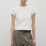 Front view of white tori top on model wearing khaki trousers and black belt, against white background.