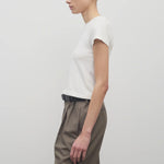 Side view of white tori top on model wearing khaki trousers and black belt, against white background.
