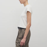 Side view of white tori top on model wearing khaki trousers and black belt, against white background.