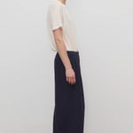 Side view of dark navy ukira pant on model wearing white t-shirt, against a white background.