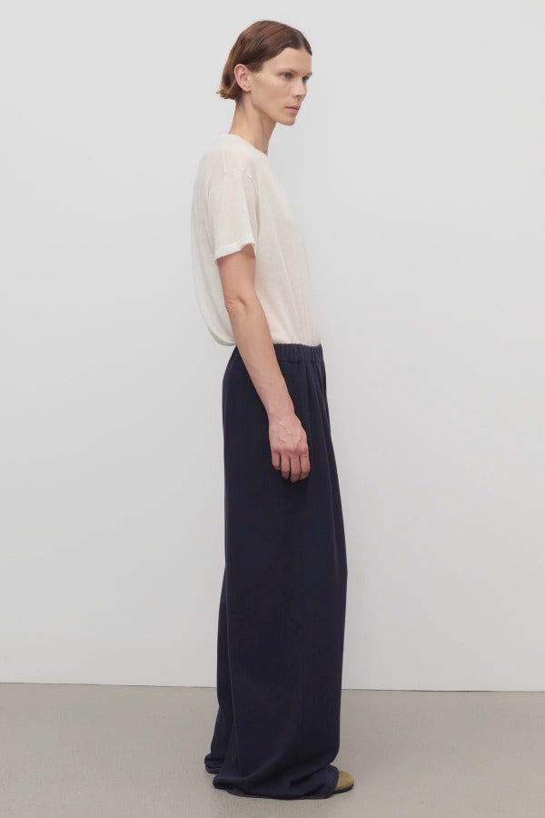 Side view of dark navy ukira pant on model wearing white t-shirt, against a white background.