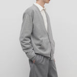 Side view of grey melange vonn cardigan on model wearing grey trousers and a white shirt, against a white background.