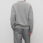 Back view of grey melange vonn cardigan on model wearing grey trousers and a white shirt, against a white background.