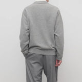 Back view of grey melange vonn cardigan on model wearing grey trousers and a white shirt, against a white background.