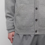 Front closeup view of grey melange vonn cardigan on model wearing white trousers and a white shirt, against a white background.