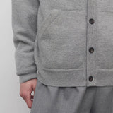 Front closeup view of grey melange vonn cardigan on model wearing white trousers and a white shirt, against a white background.