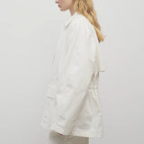 Side view of white elodianna jacket on model wearing white trousers and white shirt against a white background.