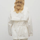 Back view of white elodianna jacket on model wearing white shirt and white trousers, against a white background.