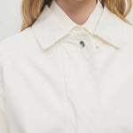 Front closeup view of white button down elodianna jacket on model wearing white shirt, against a white background.