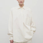 Front view of white erika shirt on model wearing white trousers, against white background.
