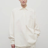 Front view of white erika shirt on model wearing white trousers, against white background.
