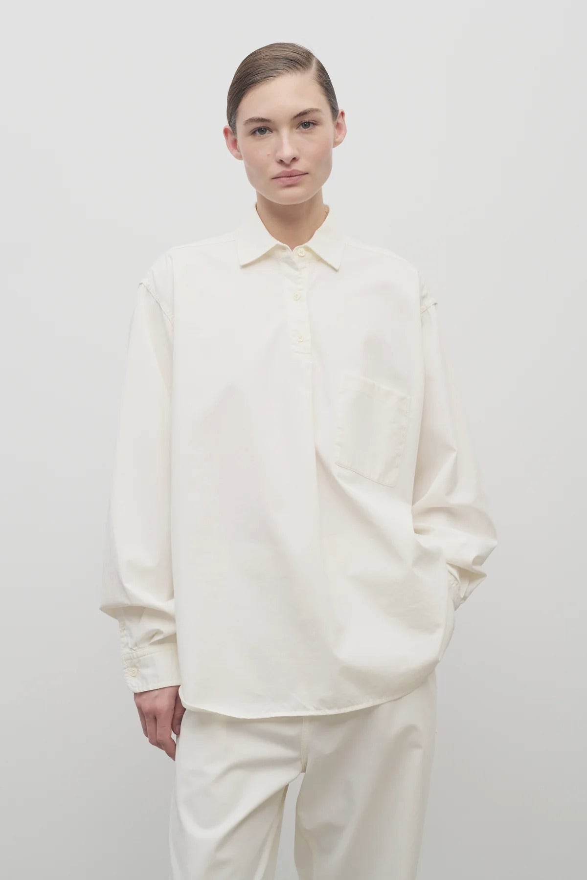 Front view of white erika shirt on model wearing white trousers, against white background.