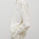 Side view of white erika shirt on model wearing white trousers, against white background.