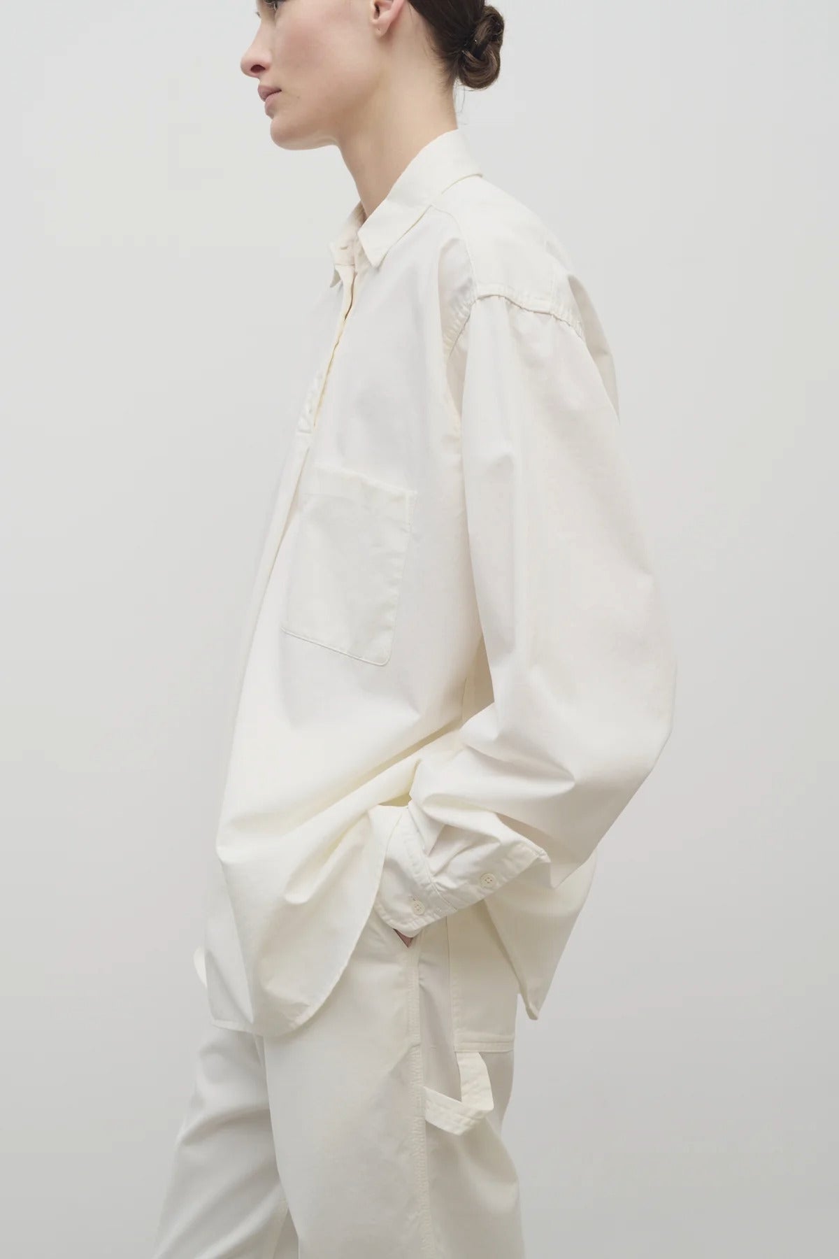 Side view of white erika shirt on model wearing white trousers, against white background.