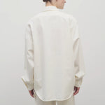 Back view of white erika shirt on model wearing white trousers, against white background.