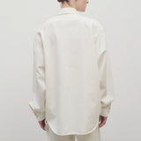 Back view of white erika shirt on model wearing white trousers, against white background.