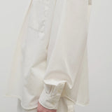Side closeup view of white erika shirt on model wearing white trousers, against white background.