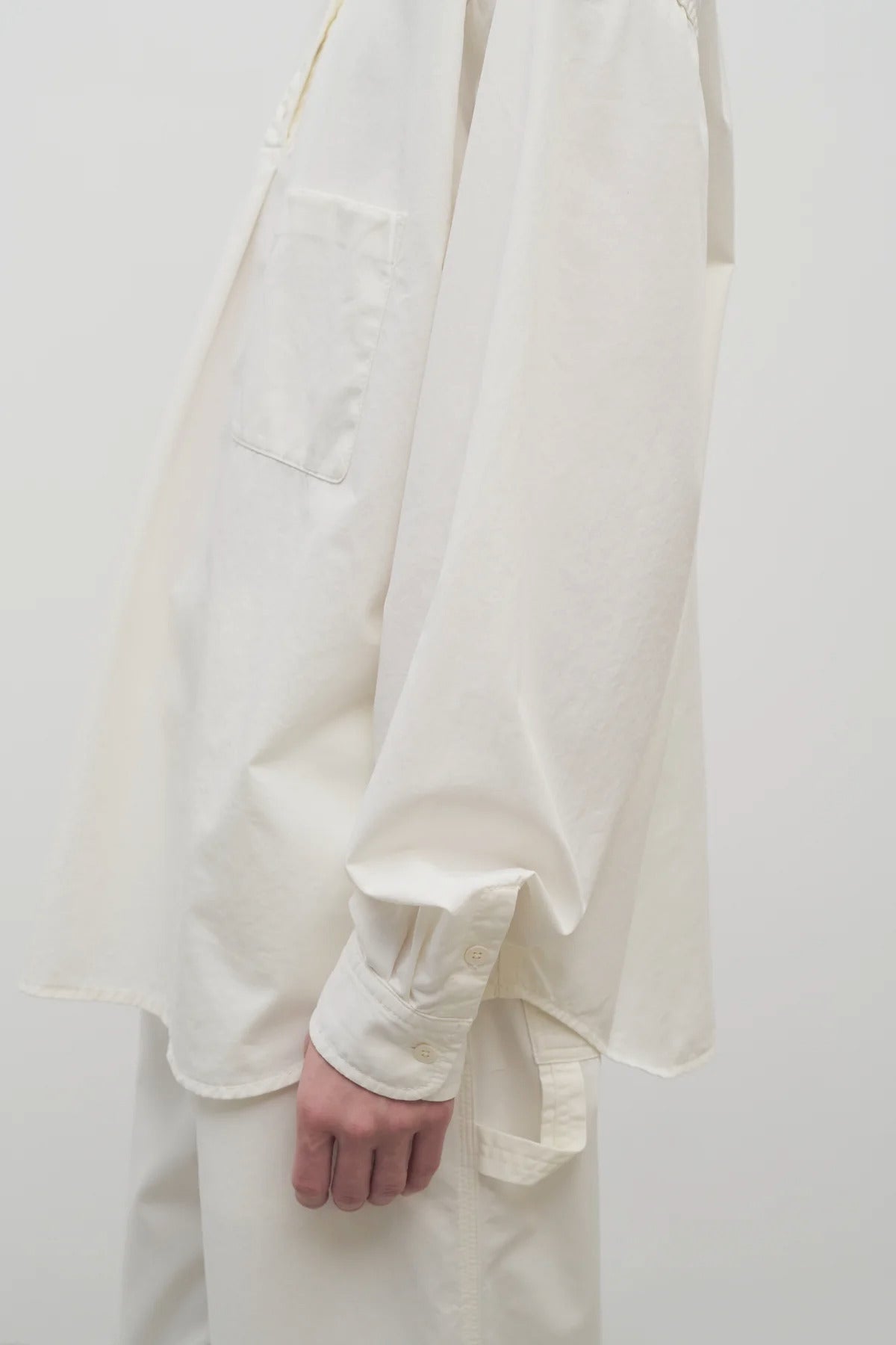 Side closeup view of white erika shirt on model wearing white trousers, against white background.