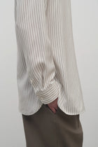 Side closeup view of Long sleeve silk shirt in white with grey on brunette haired model  worn with khaki trousers.