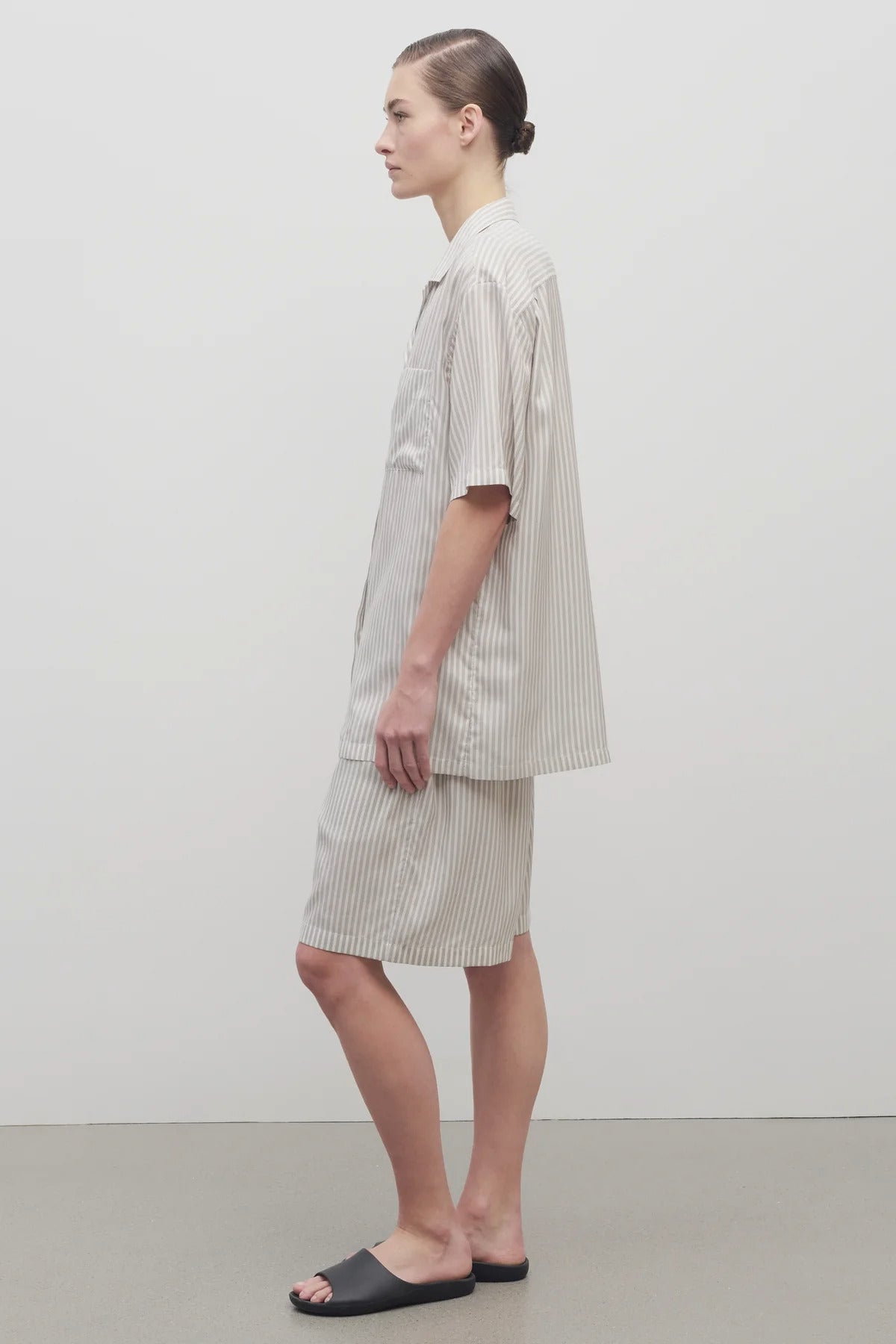 Side view of short with white background, on light brown haired model, worn with matching silk shirt and black sandals.